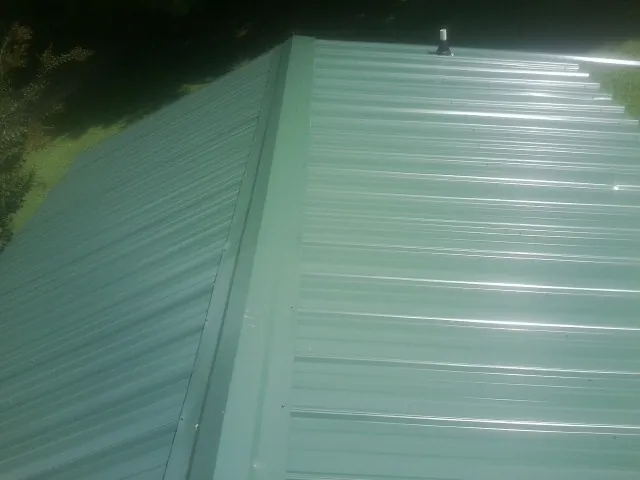 New green metal panels meeting at the ridge of a roof — Flat Roof Repair work by our crew in Snow Shoe