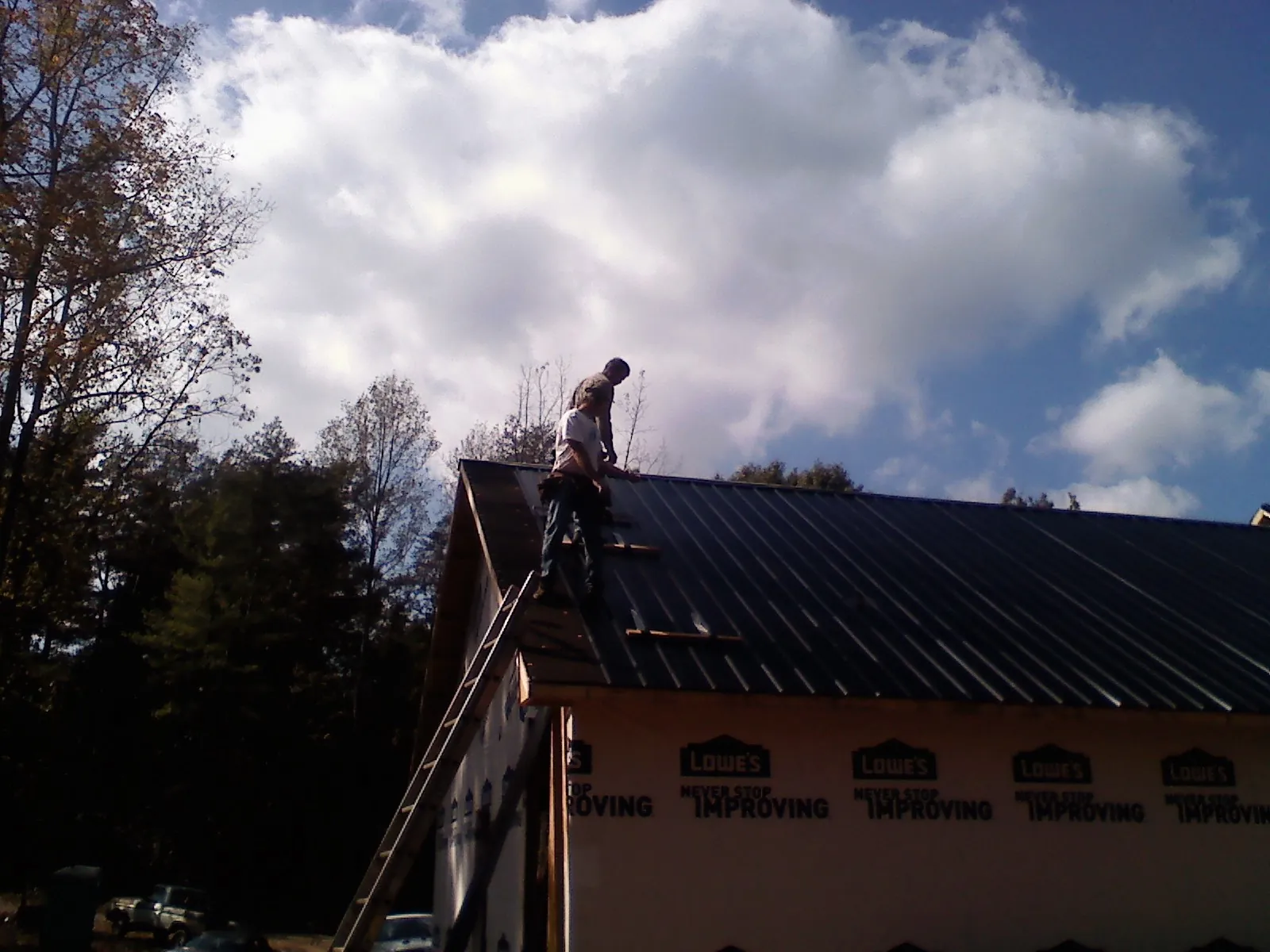 Roofer fastening dark metal panels high against a cloudy sky, from a Roof Inspection job in Snow Shoe