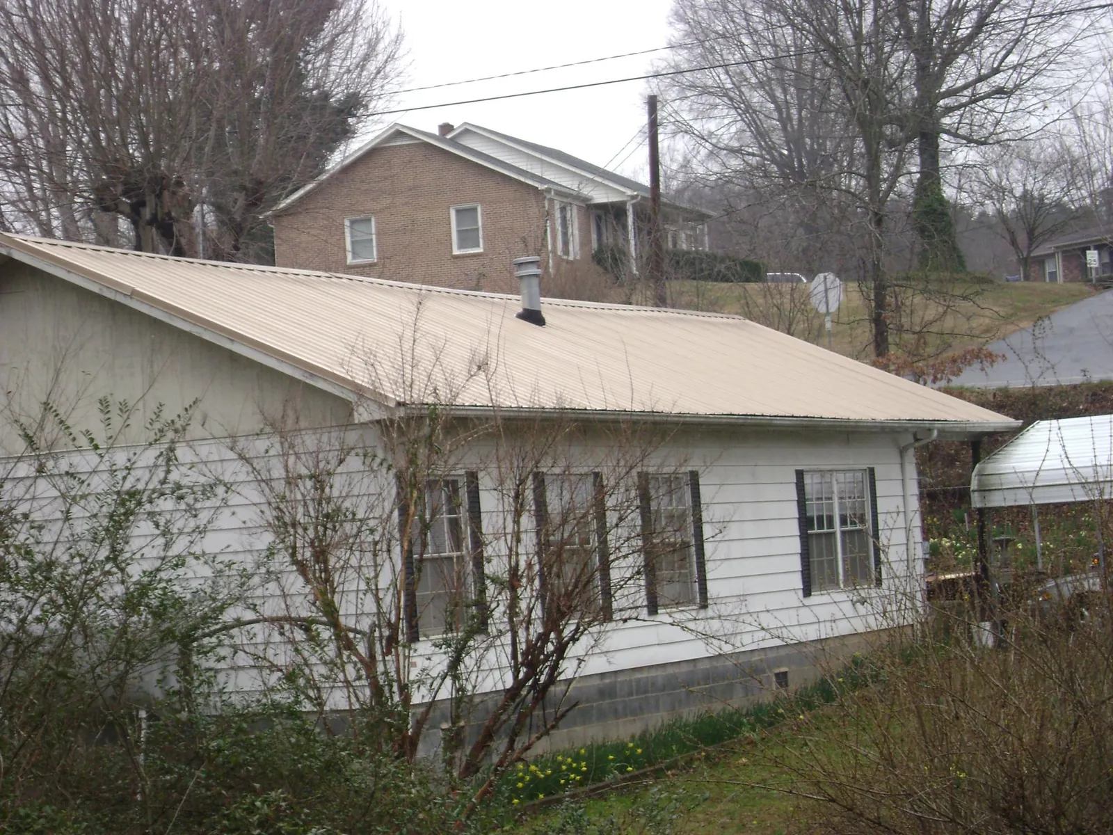 Tan metal roof on a white sided house set into a hillside — Commercial Roofing by Roofing Brothers in Snow Shoe